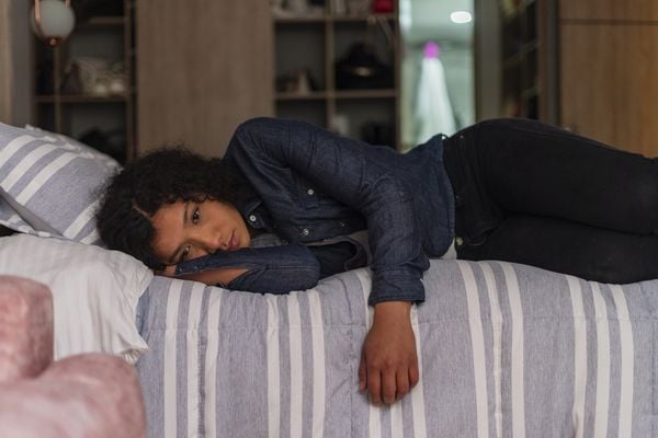 Mulher com feição triste deitada na cama