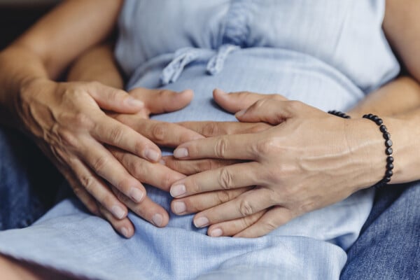 imagem aproximada das mãos de uma mulher grávida e de um homem tocando a barriga