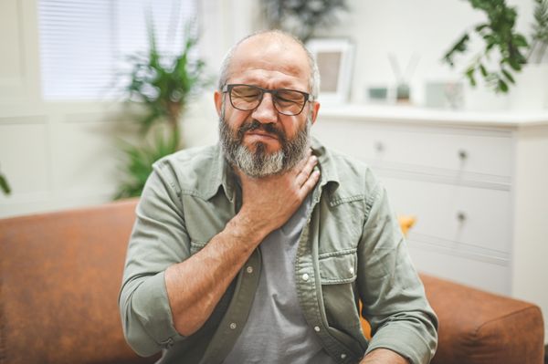 Homem com a mão na garganta sentindo desconforto