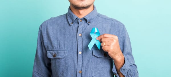 Homem com camisa jeans azul segura fita azul em frente ao peito.