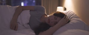Mulher deitada na cama com uma mão na cabeça tentando dormir